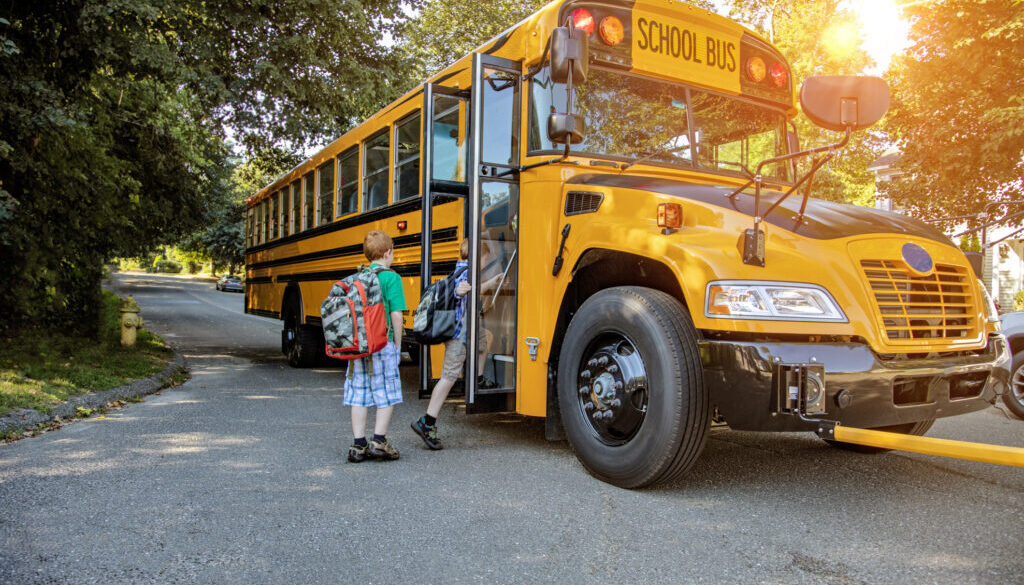 A young boy getting onto a school bus in sunshine